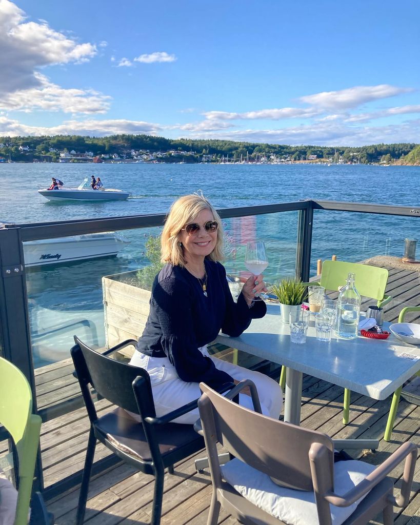 Glynis Barber sitting on a dock in front of a blue sky and blue water 
